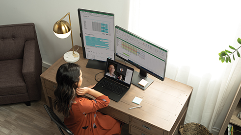 Una mujer que participa en una reunión por equipos, archivo de Excel abierto en varias pantallas en su escritorio